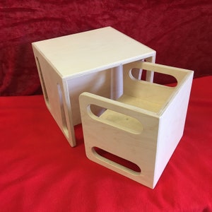 May include: A set of two wooden nesting boxes. The larger box is a cube with a square opening on one side. The smaller box fits inside the larger box and has two oval cutouts on one side.