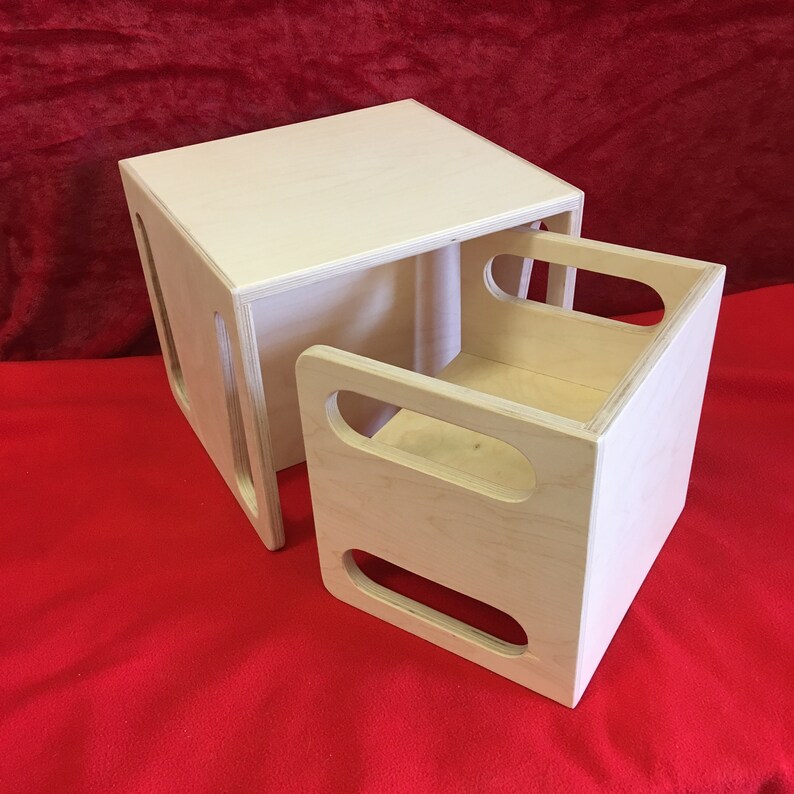 May include: A set of two wooden nesting boxes. The larger box is a cube with a square opening on one side. The smaller box fits inside the larger box and has two oval cutouts on one side.