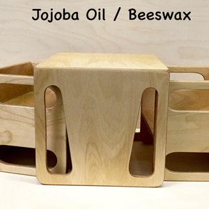 May include: Three light-colored wooden storage boxes with cut-out handles. The boxes are arranged together, with one box on top of the other two. The text "Jojoba Oil / Beeswax" is at the top of the image.