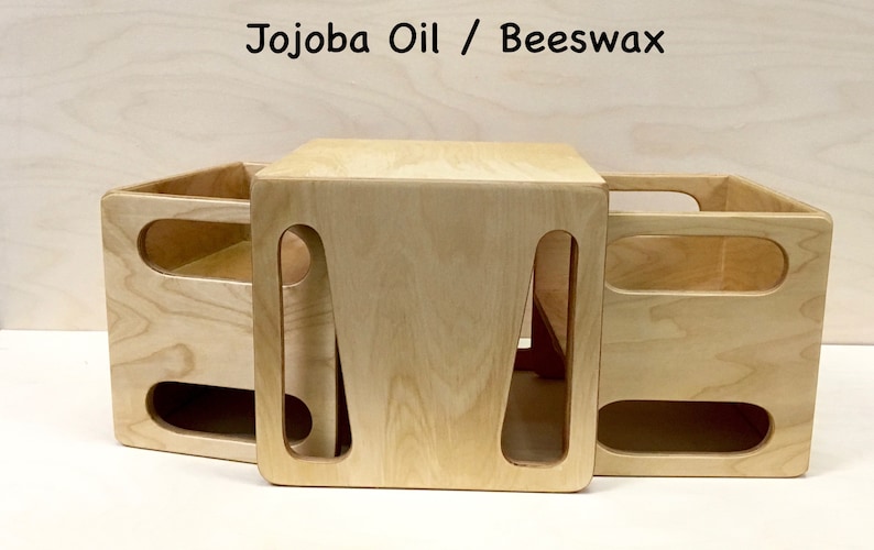 May include: Three light-colored wooden storage boxes with cut-out handles. The boxes are arranged together, with one box on top of the other two. The text "Jojoba Oil / Beeswax" is at the top of the image.