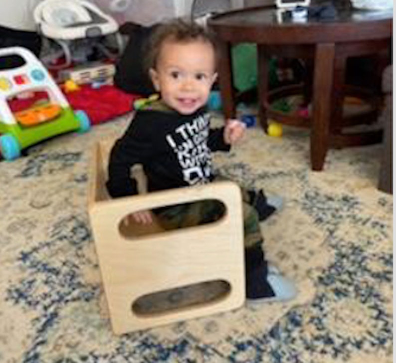May include: A young child sits on a wooden step stool with two openings. The child is wearing a black long-sleeved shirt with white lettering that says "I think I can I know I will". The child is wearing camouflage pants and has brown hair.