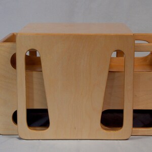 May include: A light-colored wooden storage cube with cut-out handles. The cube is made of light-colored wood and has a simple, modern design. The cube is approximately 15 inches wide, 15 inches deep, and 15 inches tall.