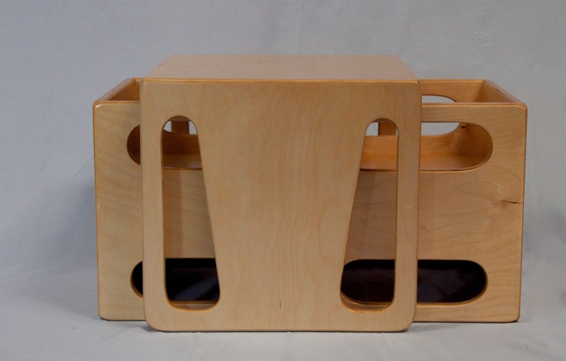 May include: A light-colored wooden storage cube with cut-out handles. The cube is made of light-colored wood and has a simple, modern design. The cube is approximately 15 inches wide, 15 inches deep, and 15 inches tall.
