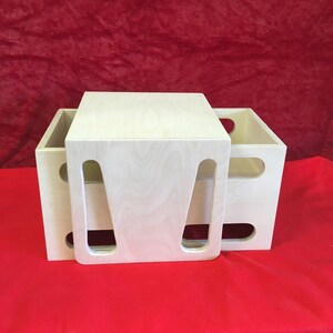 May include: Two wooden boxes with cut-out handles, stacked on top of each other. The top box is a light wood color and the bottom box is a slightly darker wood color.