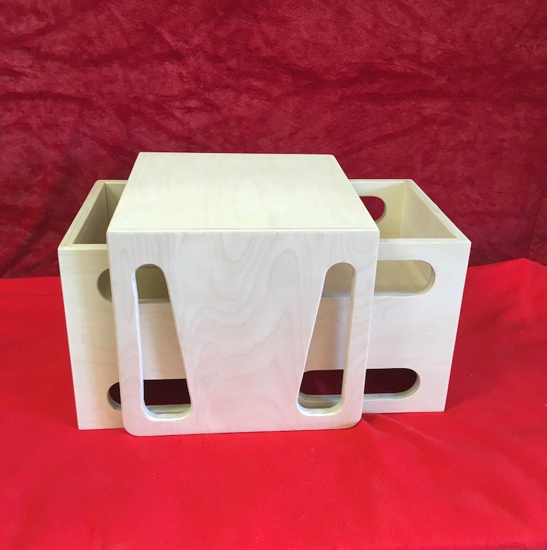 May include: Two wooden boxes with cut-out handles, stacked on top of each other. The top box is a light wood color and the bottom box is a slightly darker wood color.