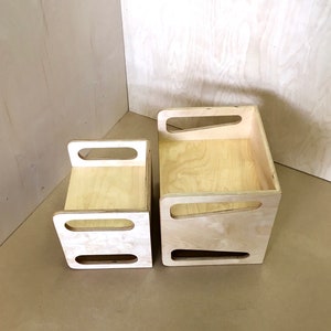 May include: Two unfinished wooden storage boxes of different sizes. Each box has a rectangular shape with cut-out handles on the sides. The wood grain is visible, and the boxes are set against a light-colored background.