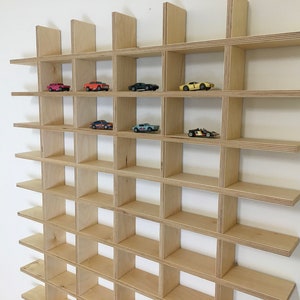May include: A light-colored, wooden wall shelf with a grid-like design. The shelf is filled with miniature toy cars of various colors. The shelf is mounted on a white wall, creating a display for collectibles.