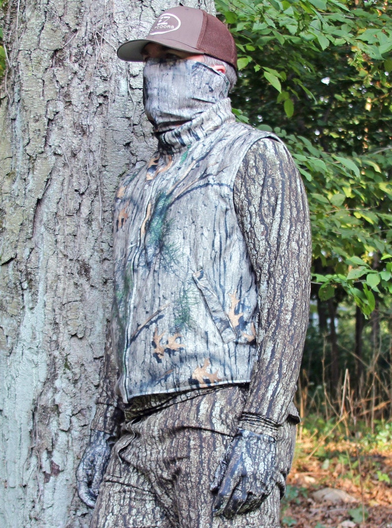 Puede incluir: Una persona con un chaleco de camuflaje y pantalones a juego con una gorra de b&eacute;isbol marr&oacute;n. La persona est&aacute; de pie frente a un &aacute;rbol con un patr&oacute;n de corteza.