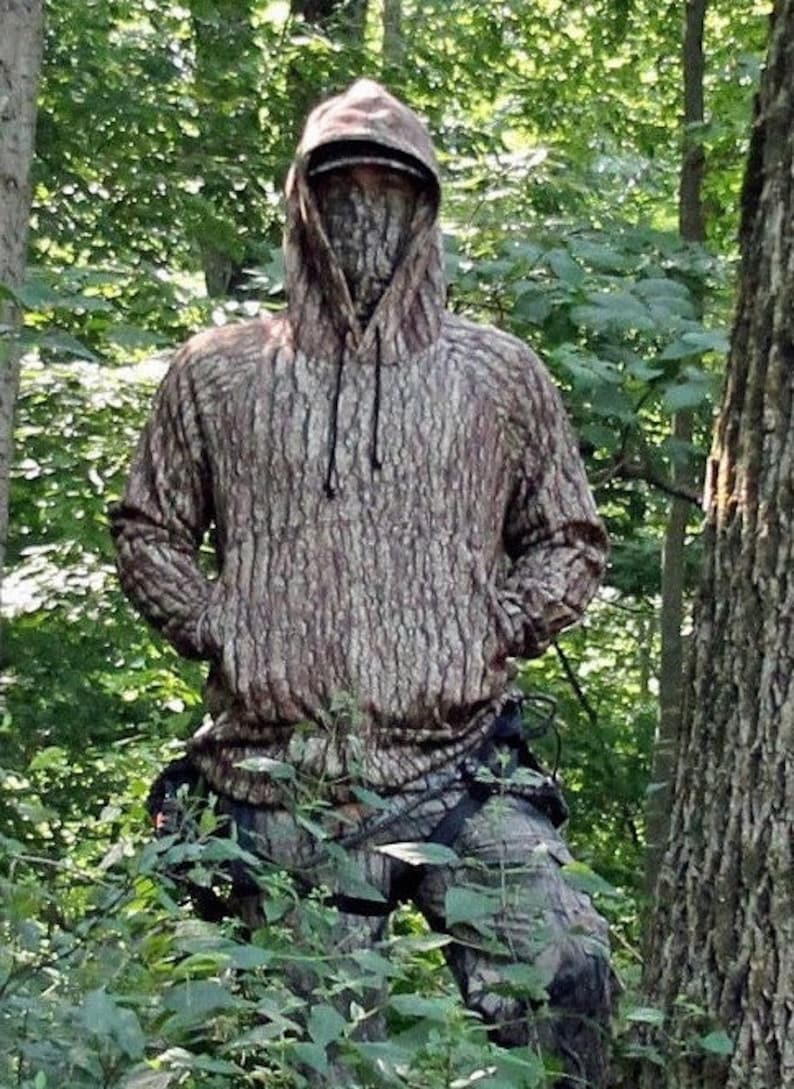 May include: A brown and tan camouflage hoodie with a drawstring hood. The hoodie is made of a soft, comfortable material and features a realistic tree bark pattern.