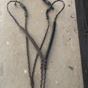 May include: A black and brown braided lanyard with a black and green braided lanyard attached to it. The lanyard has a black plastic clip on one end and a brown loop on the other end.