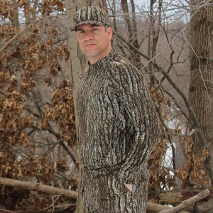 May include: A camouflage print long-sleeve shirt with a high neck and a matching camouflage print cap. The shirt and cap are designed to blend in with a woodland environment.