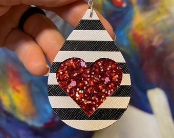 May include: Black and white striped teardrop-shaped earrings with a red glitter heart in the center.