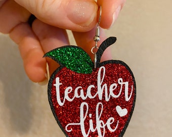 May include: Red glitter apple-shaped earrings with a green glitter leaf and the text "teacher life" in white with a small white heart.
