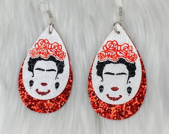 May include: A pair of red glitter teardrop-shaped earrings with a white background and a black and white image of Frida Kahlo with a flower crown.