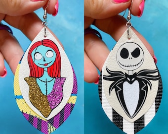 May include: A pair of dangle earrings featuring a layered design. One earring has a colorful illustration of Sally from the Nightmare Before Christmas. The other earring has a black and white illustration of Jack Skellington from the Nightmare Before Christmas.