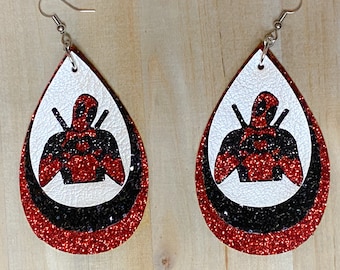 May include: A pair of red, black, and white teardrop-shaped dangle earrings with a glitter finish. The earrings feature a silhouette of Deadpool.