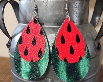 May include: Watermelon-themed dangle earrings with red and green glitter. The earrings are shaped like teardrops and have a black watermelon seed pattern.