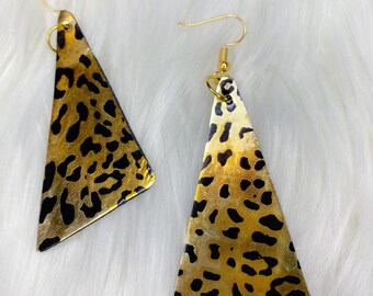 May include: A pair of gold and black triangle-shaped earrings with a leopard print pattern.