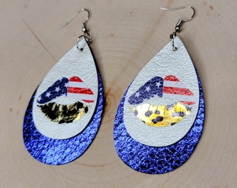 May include: A pair of teardrop-shaped earrings with a blue glitter background. The top layer is white leather with a red, white, and blue lip print. The bottom layer is gold foil with a lip print.