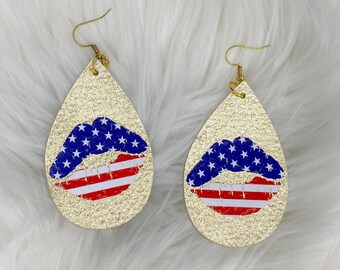 May include: Gold glitter teardrop earrings with a red, white, and blue lip design. The lip is decorated with stars and stripes.