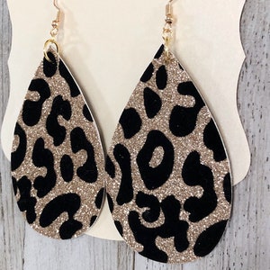 Puede incluir: Un par de pendientes en forma de l&aacute;grima con purpurina dorada y estampado de leopardo negro.
