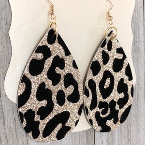Puede incluir: Un par de pendientes de gota de oro con purpurina y estampado de leopardo negro.