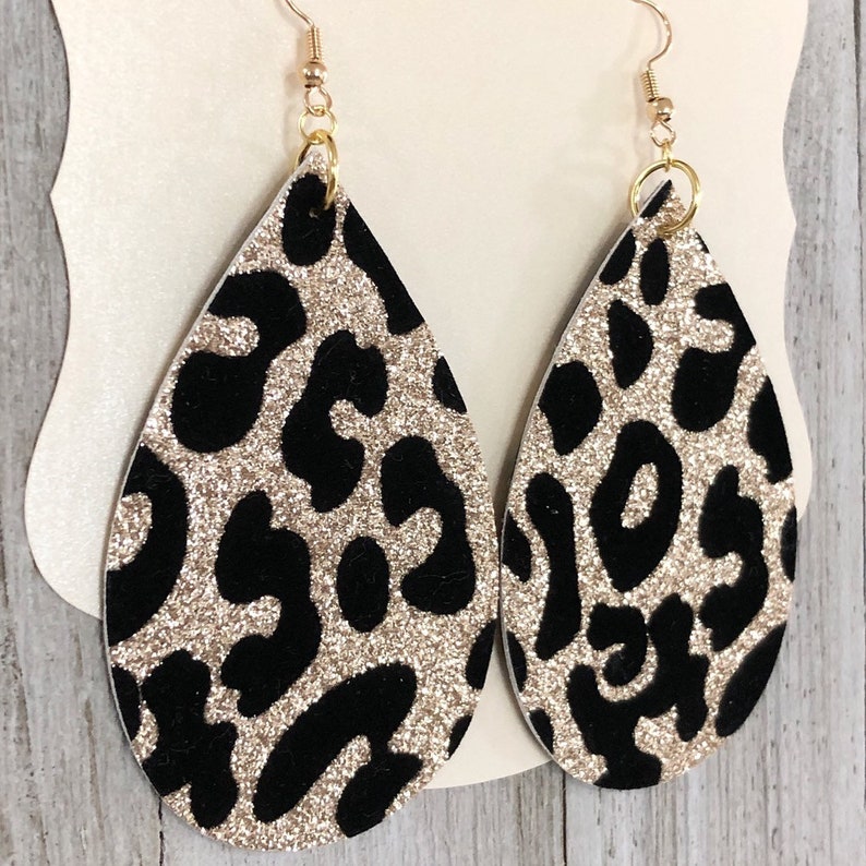 Puede incluir: Un par de pendientes de gota de oro con purpurina y estampado de leopardo negro.