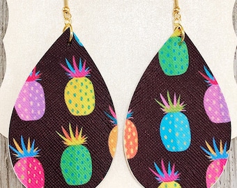 May include: A pair of teardrop-shaped earrings with a black background and a colorful pineapple pattern. The earrings have gold hooks.