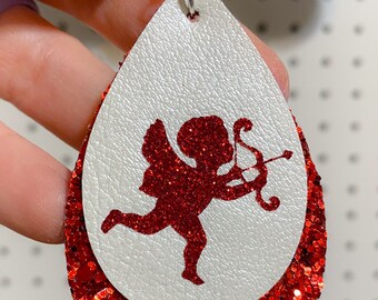 May include: Red glitter teardrop shaped earrings with a white leather overlay featuring a red glitter cupid silhouette.