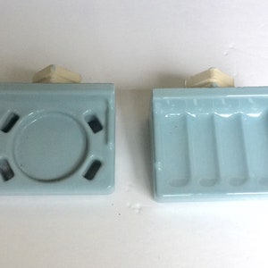 May include: Two light blue ceramic soap dishes. One dish has a round depression for a bar of soap. The other dish has three rectangular depressions for bars of soap.