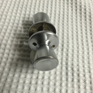 May include: A silver door knob with a round handle and a keyhole. The knob is attached to a round plate with two screws.