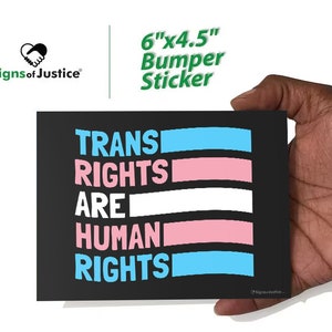 May include: A black bumper sticker with the text "TRANS RIGHTS ARE HUMAN RIGHTS" in white, pink, and blue. The sticker is 6" x 4.5" and features the "Signs of Justice" logo. The design incorporates the colors of the transgender pride flag.