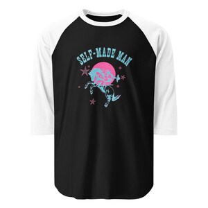 May include: A black and white raglan t-shirt with three-quarter length sleeves. The front features a graphic of a light blue rearing horse in front of a solid pink circle, surrounded by small stars and the text SELF-MADE MAN in light blue.