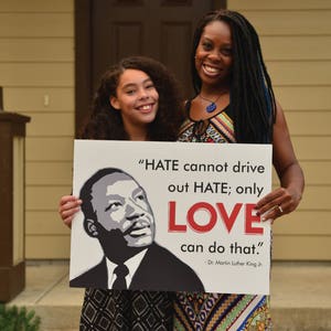 May include: Two people, a woman and a young girl, hold a sign with a quote from Dr. Martin Luther King Jr. The sign reads, "HATE cannot drive out HATE; only LOVE can do that." - Dr. Martin Luther King Jr.