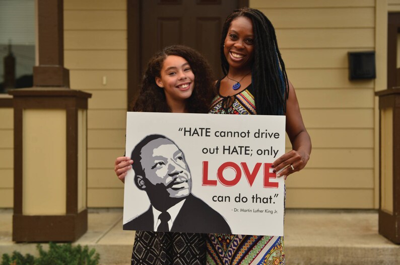 May include: Two people, a woman and a young girl, hold a sign with a quote from Dr. Martin Luther King Jr. The sign reads, "HATE cannot drive out HATE; only LOVE can do that." - Dr. Martin Luther King Jr.