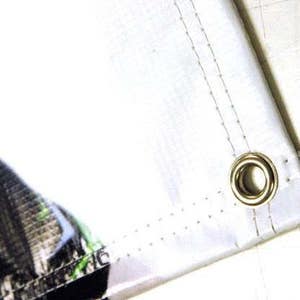 May include: Close-up of a white fabric banner with a metal grommet. The banner has a stitched edge and a subtle pattern of small dots.