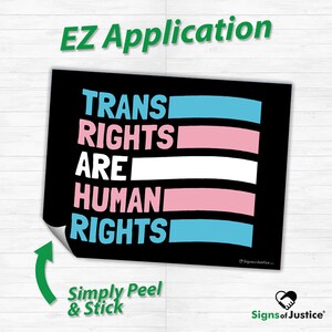 May include: A black sticker with the text "TRANS RIGHTS ARE HUMAN RIGHTS" in white, pink, and blue. The sticker has a peel-off corner and the words "EZ Application" and "Simply Peel & Stick" are also visible.