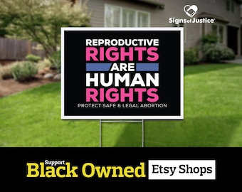 May include: Black and white yard sign with the text "Reproductive Rights Are Human Rights" in pink and blue lettering. The sign also includes the text "Protect Safe & Legal Abortion" in black lettering. The sign is on a green lawn in front of a house. The sign is for sale on Etsy.