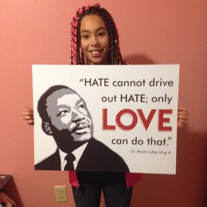 May include: A young person holding a sign with a quote from Dr. Martin Luther King Jr. The quote reads "HATE cannot drive out HATE; only LOVE can do that."
