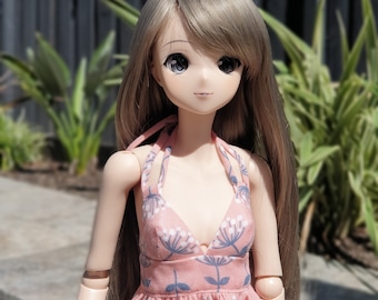 May include: A doll with long brown hair wearing a pink and blue floral dress. The doll has large brown eyes and a light complexion.