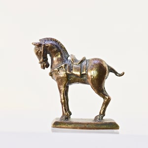 May include: A small, bronze horse figurine with a saddle. The horse is standing on a rectangular base.