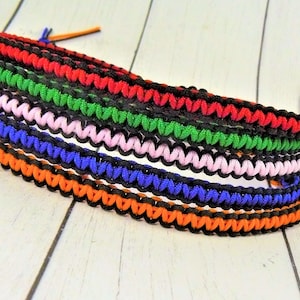 May include: A set of six colorful friendship bracelets, each with a black braided border. The bracelets are made of woven string in orange, blue, pink, green, red, and black.