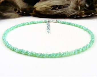 May include: A delicate choker necklace made with tiny, light green glass beads. The necklace has a silver chain clasp.