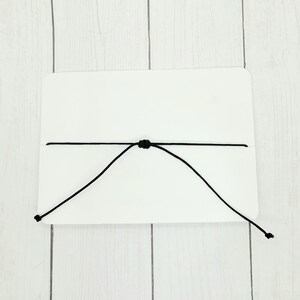 May include: A white card with a black string tied around it, forming a loop.