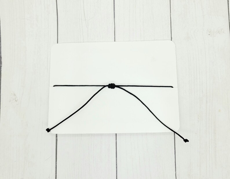 May include: A white card with a black string tied around it, forming a loop.
