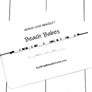 May include: A white card with black text that reads "Morse Code Bracelet Beach Babes" and a black string bracelet with white beads. The text at the bottom of the card reads "DjsWrapBracelets.etsy.com".