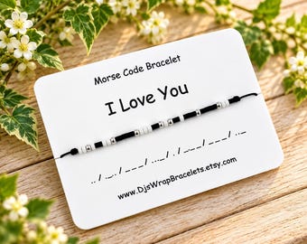May include: A black cord bracelet with white and silver beads representing Morse code, attached to a white display card. The card features the text Morse Code Bracelet, I Love You, and the website address www.DjsWrapBracelets.etsy.com.