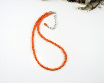 May include: A simple orange beaded necklace with a silver chain clasp.