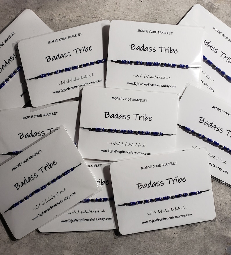 May include: Multiple white cards with the text "Morse Code Bracelet Badass Tribe" and a blue and silver beaded bracelet on each card. The text "www.DjsWrapBracelets.etsy.com" is printed on each card.