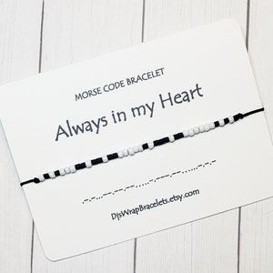 May include: Black and white beaded bracelet with a black string. The bracelet spells out "Always in my Heart" in Morse code. The card reads "Morse Code Bracelet Always in my Heart" and includes the website "DjsWrapBracelets.etsy.com".